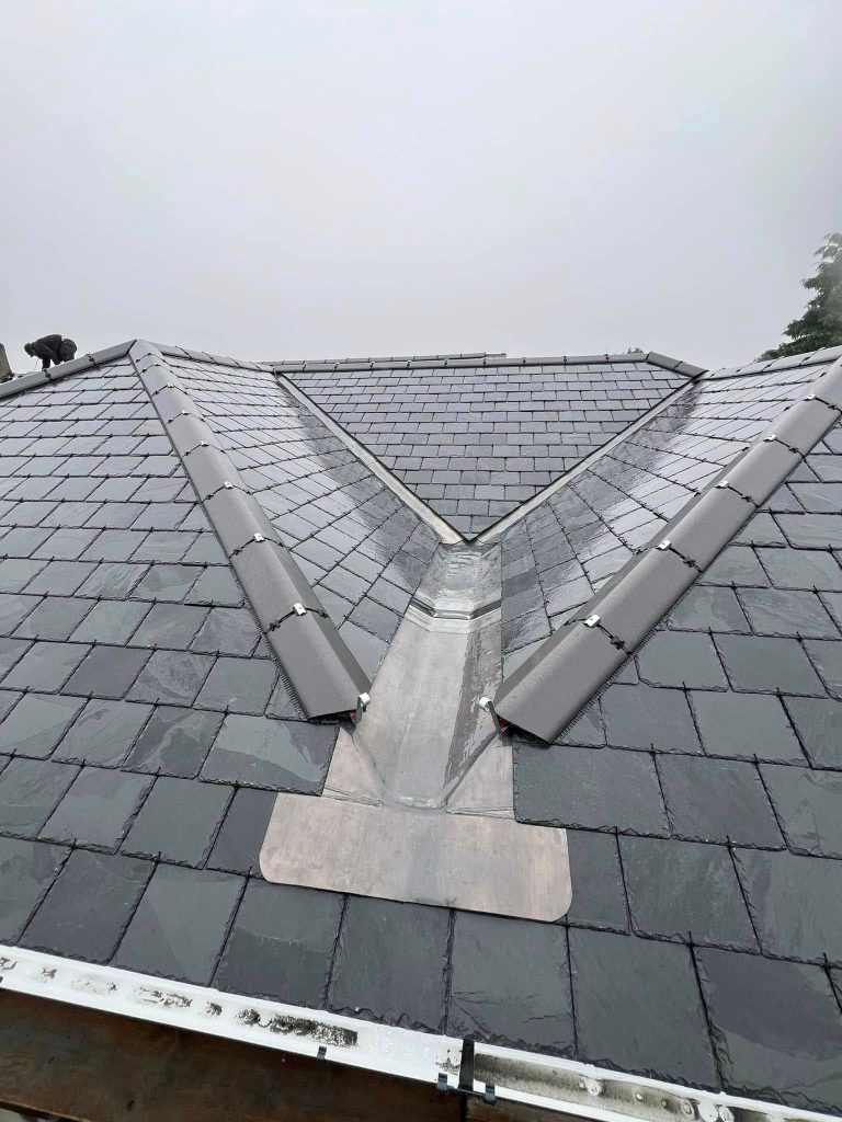 A newly installed slate roof with clean lines, gray tiles, and a metal valley flashing at the intersection of two roof sections on a foggy day.